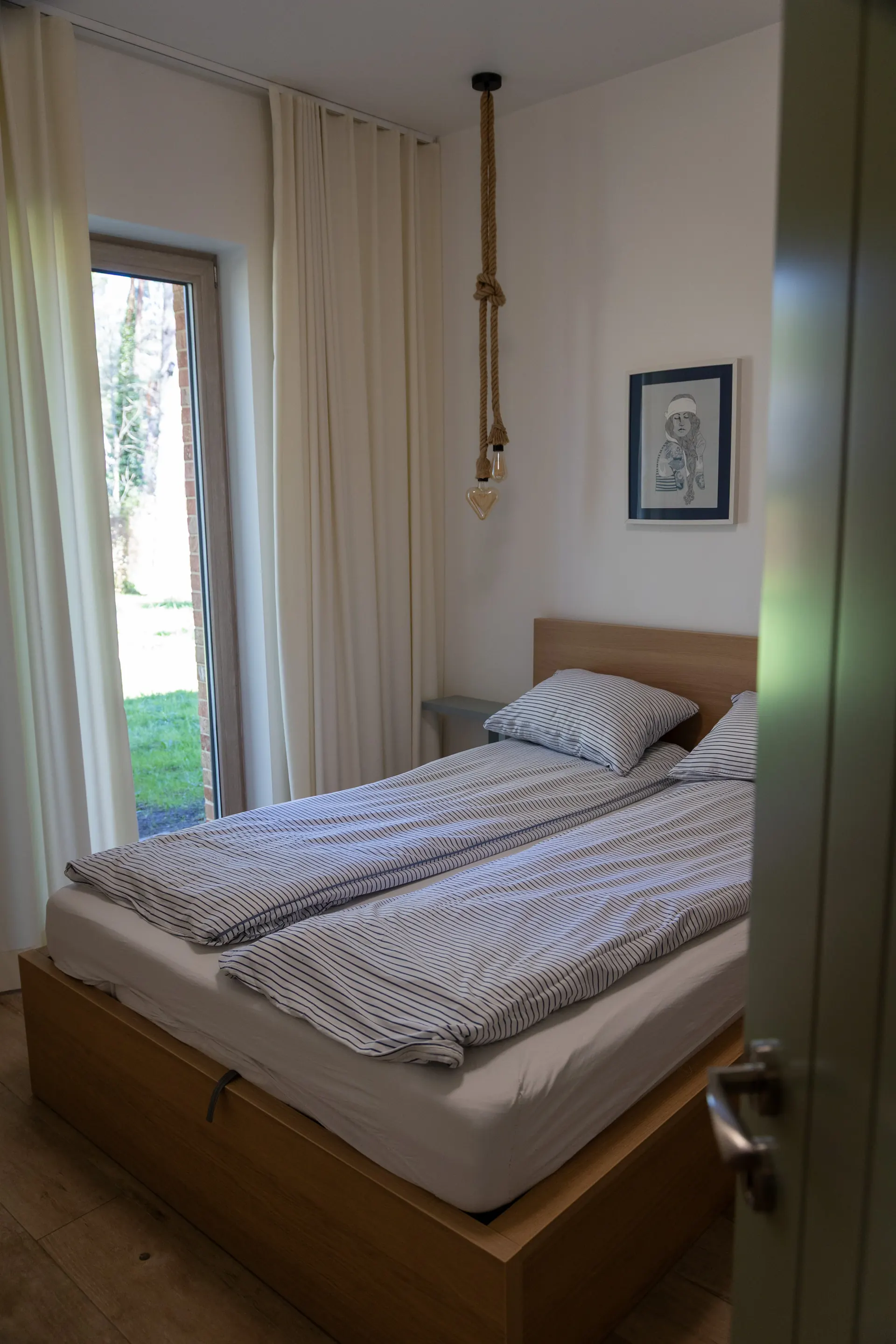 Mała sypialnia z drewnianym łóżkiem i wiszącą lampą loftową na lince — Apartament 3 Poezja Ciszy Dębki
